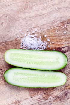 Sliced along a ripe green cucumber, salt and vegetables on a cutting board, closeup