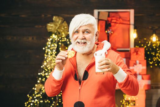 Santa in home. Santa picking cookie and glass of milk at home. Christmas Beard style. Portrait of Santa Claus Drinking milk from glass and holding cookies