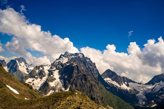 From below white clouds floating on blue sky over mountain ridge covered with snow on sunny day in nature