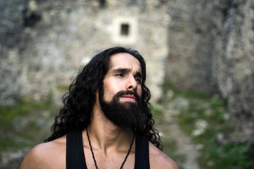 Middle-aged sexy man with long hairstyle. Sad frustrated man with long dark wavy hair and beard looking far away. Portrait of handsome man with disappointed face