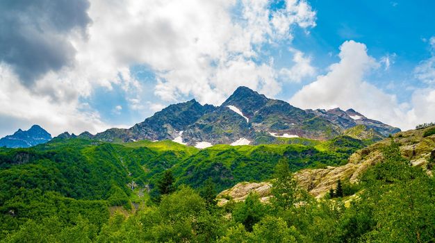 Mighty mountains with snow and green array in cloudy weather.