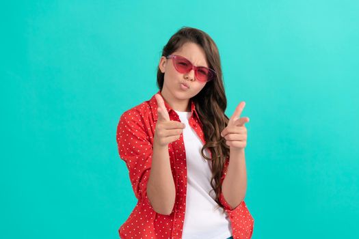 cool kid with curly hair in sunglasses. beauty and fashion. female fashion model. pretty look of young girl. portrait of child pointing finger on camera on blue background. express positive emotions.