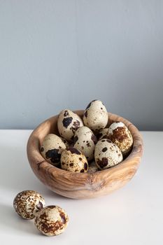 Speckled quail eggs in a wood bowl on a farm table in the kitchen.