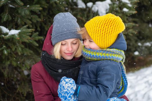 Mother and son enjoying winter outdoors. Pine trees covered with snow. A beautiful family walks through the winter snowy forest. Holidays, christmas, happiness together, childhood in love