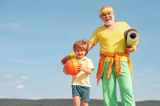 Joyful old-aged man and cute little boy practicing sport and healthy lifestyle over sky background. Sports education