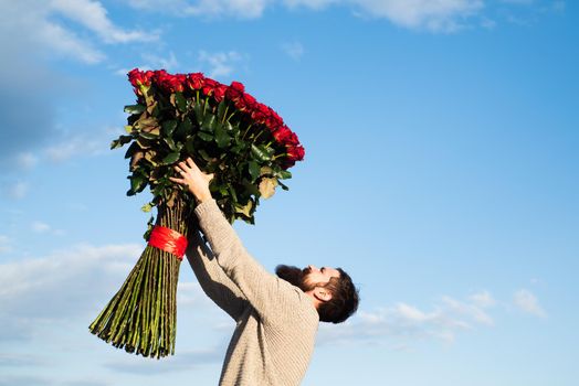 Bearded man with red rose bouquet. Valentine's day. Gift with love. Handsome man on background sky. Gift on Valentine's day