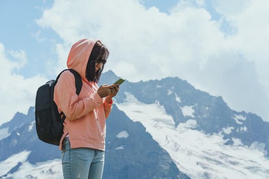 Woman tourist browsing mobile phone against cloudy sky on sunny day in mountainous terrain.