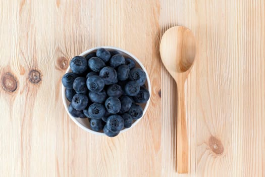 ripe large blueberry lying in a plate on a wooden table, to the right of the berries lies a wooden spoon, closeup photo, top