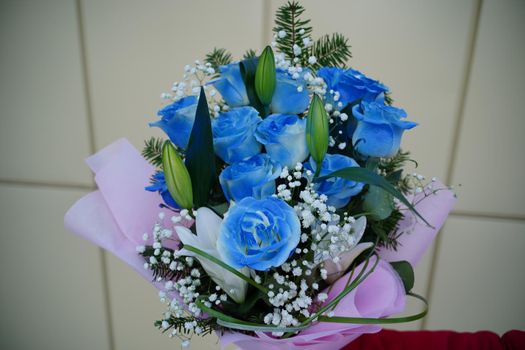 Close up of woman's hand holds colorful bouquet of flowers. Unrecognizable female holding flower composition of blue roses and white lilies in wrapping paper