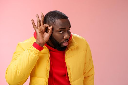 Curious funny charismatic black bearded guy bending forward hold hands ear eavesdropping wanna overhear girlfriend conversation behind door standing curious gossiping pink background.