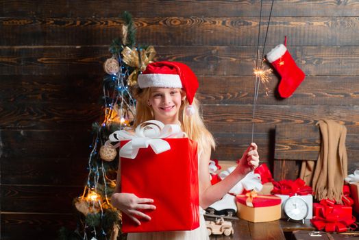 Funny kid holding Christmas gift. Christmas kids. Merry Christmas and Happy Holidays. Happy small teenager in Santa hat with present have a Christmas. Winter evening at home