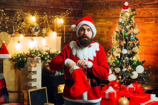 Christmas stockings. Santa winter portrait. Sexy Santa man posing on vintage wooden background. Bearded modern Santa Claus in knitted sweater