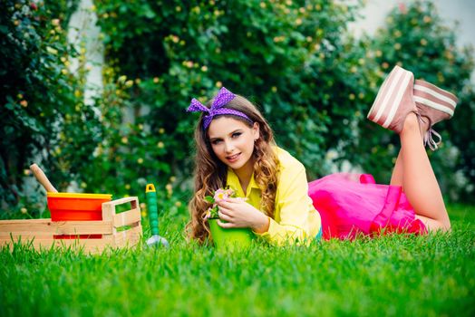 Beautiful girl lie on grass at her spring garden. Young pretty woman enjoy spring nature and take care about her plants. Eco garden worker concept. Garden woman with tools