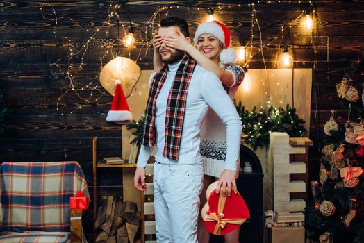 Cheerful smiling girlfriend covers her boyfriend's eyes preparing for him new year or christmas gift. Happy new year. Christmas eve. New Year. Home. Celebrating Christmas together concept