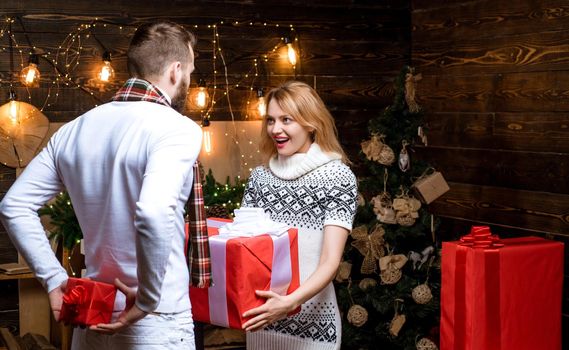 Bright New Years interior. Christmas interior. Positive delighted loving couple giving each other Christmas gifts. Happy New Year. Christmas gifts. Celebrating New Year together