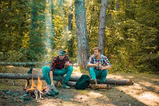 Summer vacation forest. Good day for spring picnic in nature. Spring or autumn camping. Friends men hikers watching fire together on camp. Happy young male friends having picnic