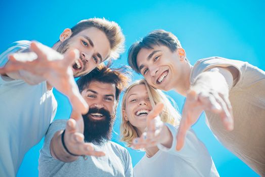 Excited people. Group of happy cheerful smiling friends offer their hands down to the camera at clear blue sky background. Summertime and friendship concept. Teammates gather together and have fun