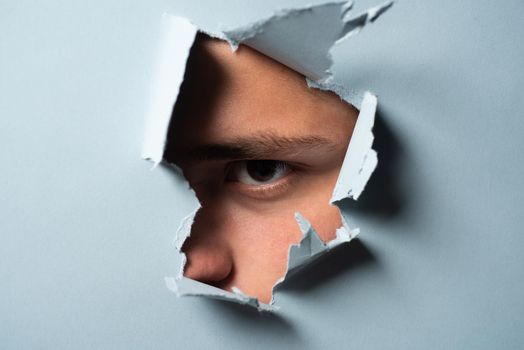 Man looking through paper. A jealous husband. Hole torn in paper with the eye of boy. Portrait of man looking through the hole in white paper. Distrustful look. Spy eye. Man's curiosity and gossip