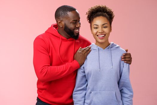 Supportive boyfriend congratulating girlfriend win first prize feel proud touching girl shoulder saying encouraging pleasant words smiling look caring lovely grinning, standing pink background.