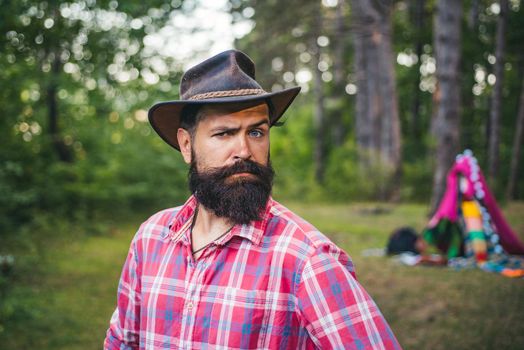 Guy in forest. Handsome bearded male. Natural background. Brutal brunette bearded man in hat on a background of trees. Mature hipster with beard. brutal man with beard