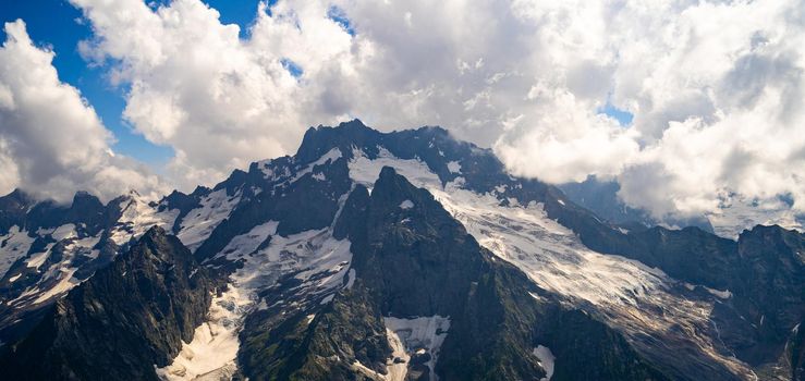 From below white clouds floating on blue sky over mountain ridge covered with snow on sunny day in nature