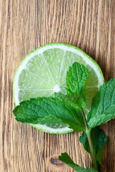 piece of green sour lime with mint leaves lying on it, photo closeup on a wooden table