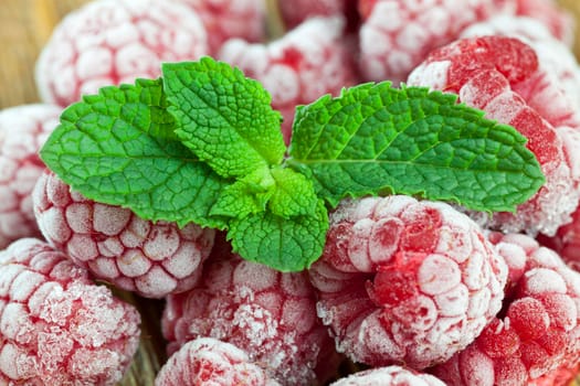 freshly frozen and frosted berries ripe red raspberries in a heap, on berries is a green leaf of fresh mint green, dessert