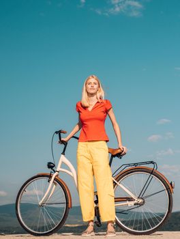 Pretty blonde woman enjoy her walk with bike. Cycling concept. Beautiful woman took a break while riding her vintage bicycle at good sunny day. Summer holidays and carefree time