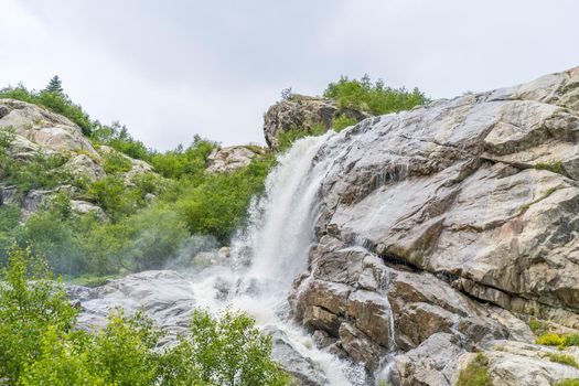 Rapid water stream falling from rocks against blue sky on sunny summer day in countryside