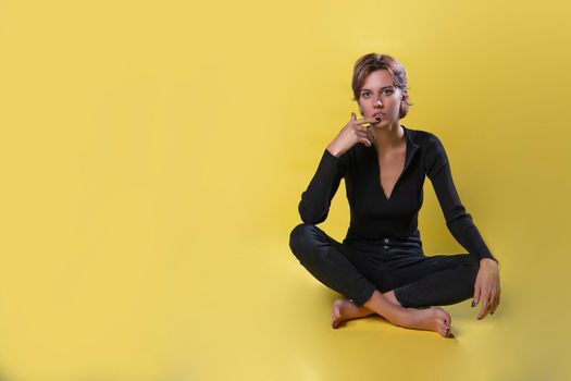 The girl sits on a yellow background in black clothes with black nails brooding, beautiful blonde on the right