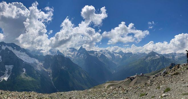 From below white clouds floating on blue sky over mountain ridge covered with snow on sunny day in nature