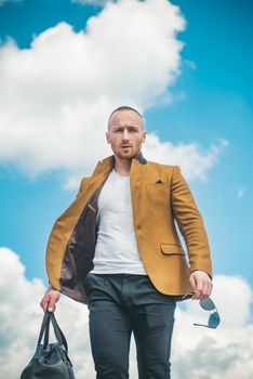 Brutal hipster boy. Lifestyle people concept. Side view portrait of confident bearded man in white t shirt.Portrait man with bag and glasses. Isolated sky background