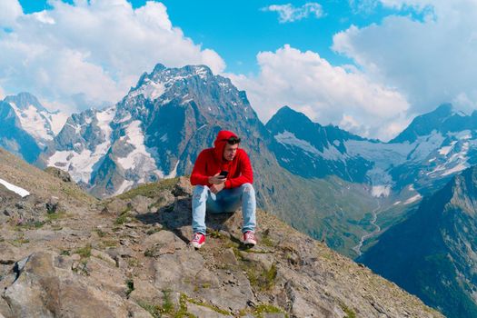 Male traveler using mobile phone against cloudy sky on sunny day in mountainous terrain