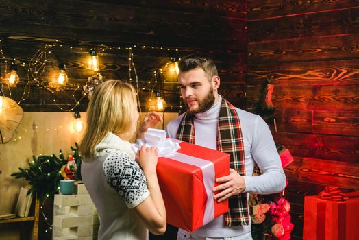 Young couple in love sitting next to a nicely decorated Christmas tree exchanging Christmas presents. Romantic couple exchanging Christmas gifts at home. New Year eve