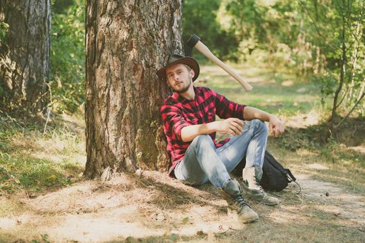 Woodcutter with axe in the summer forest. Illegal logging continues today. Lumberjack standing with axe on forest background