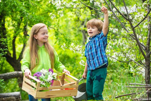 Childhood and growing up. Children play in spring garden. Little cute boy rise his hand and girl looking at him. Young generation of tree huggers and nature lovers. Childchood and outdoor leisure concept