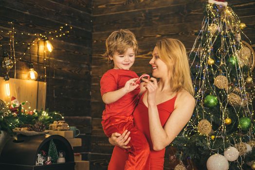 Happy smiling woman in sexy red dress cradles child in her arms at beautiful decorated background. Portrait of happy mother and adorable baby celebrate Christmas