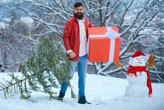 Man in Christmas dress with gift near the Christmas background. Happy father with Christmas gift over winter snowman background
