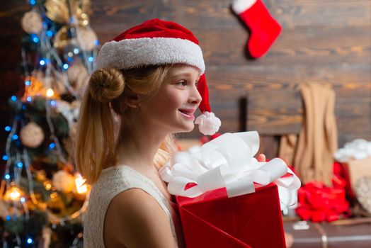 Happy Little girl with a Christmas present on wooden background. Christmas children. Joyful teenager looking at camera in Christmas at home. Christmas teenager - happiness concept