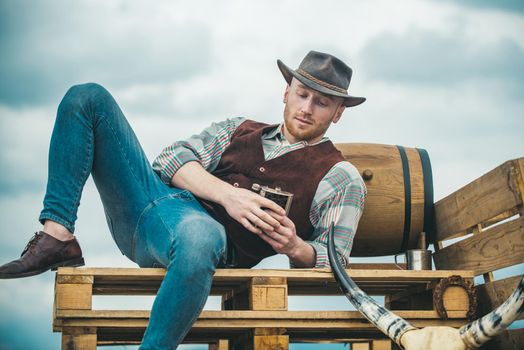 Example of true masculinity. Cowboy wearing hat. Western life. Unshaven guy in cowboy hat and plaided shirt drinking alcohol. Handsome bearded macho man. Men beauty standard