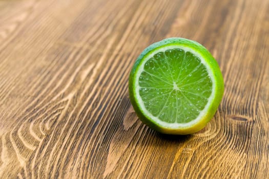 photograph of half a green lime on a wooden table board. Brown background, focus on bright fruit