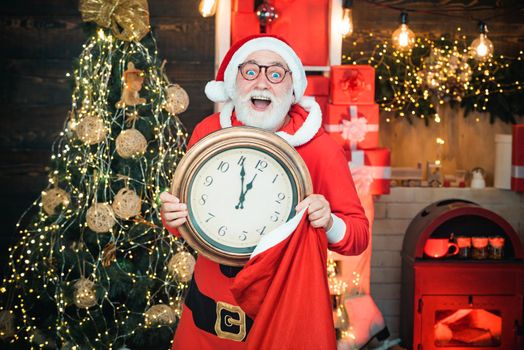 Santa Claus holding clock with countdown to Christmas or New Year Santa Claus in wooden home interior showing time on a clock