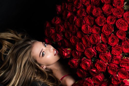 Beautiful woman with red roses. Gift with love. Beautiful smiling girl holding large bouquet of red roses on black background. Beautiful woman with red rose bouquet