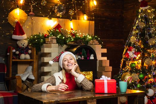 Blonde girl wearing winter sweater writes a letter to Santa Claus. Gifts for winter holidays at fire place. Happy christmas. Christmas time. Childhood memories. New Year attributes