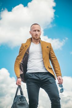 Serious young man. Bag and glasses. Portrait of handsome young serious confident young guy in white t shirt. Handsome young man isolated. Stylish bearded man. Isolated on sky