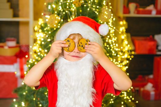 Santa - funny child picking cookie. Santa boy child eating cookies and drinking milk. Santa Claus holding Christmas cookies and milk against Christmas tree background