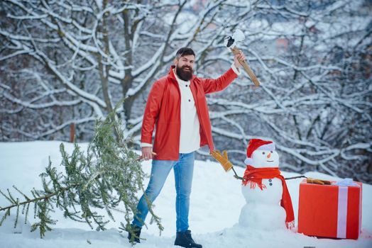 Funny Santa man posing with axe and Christmas tree. Hipster woodsman with Christmas tree. A handsome lumber with a beard carries a Christmas tree