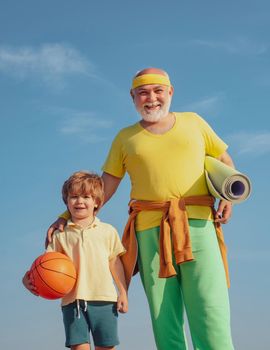 Rehabilitation. Grandfather and son doing exercises. Senior man and cute little boy exercising on blue sky background - isolated