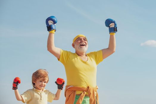 Boxer grandfather and child with blue boxing glove on blue sky background - isolated. Fighter. Funny bearded man - grandfather with child boy standing in boxing pose