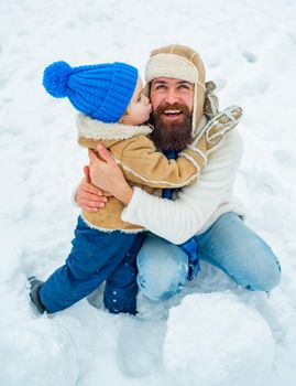 Son hugs his dad on winter holiday. Dad and baby son playing together outdoors. Happy child playing with snowball against white winter background